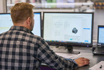 A technical employee is looking at a technical drawing of a plastic machine part on his computer. 