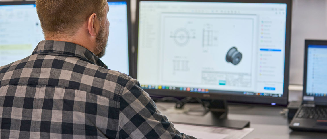 En teknisk medarbejder tjekker en teknisk tegning af en plast maskindel på sin computer. 