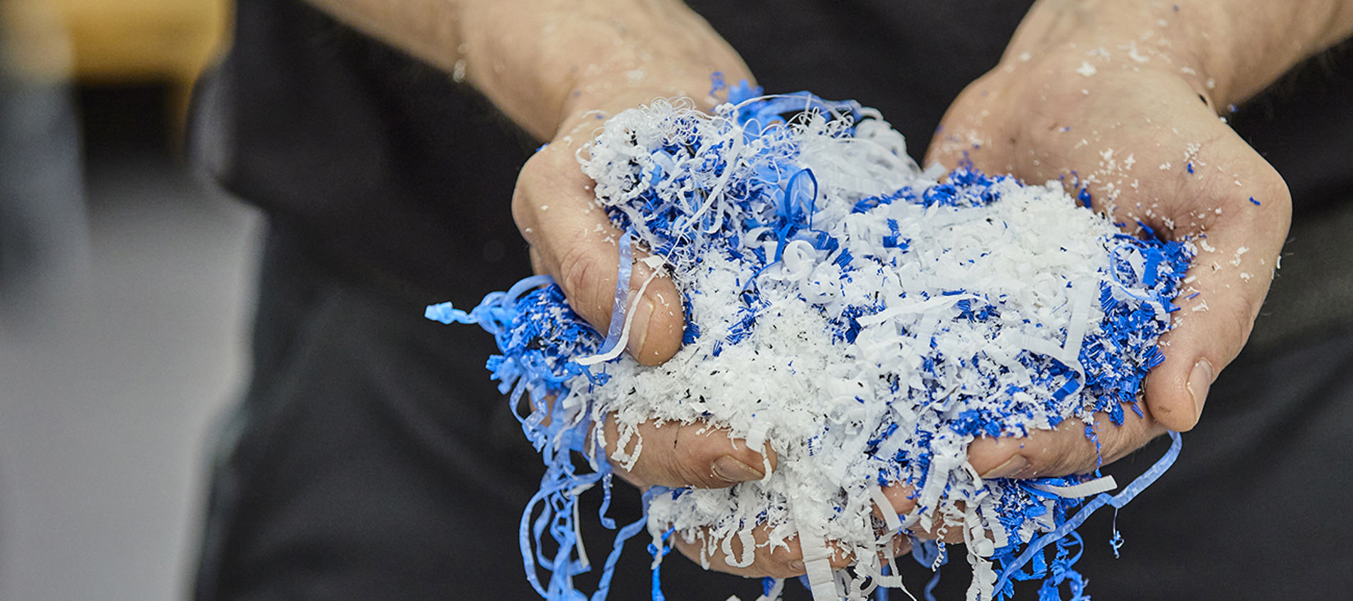Hænder holder spåner fra spåntagende bearbejdning i blå og hvid