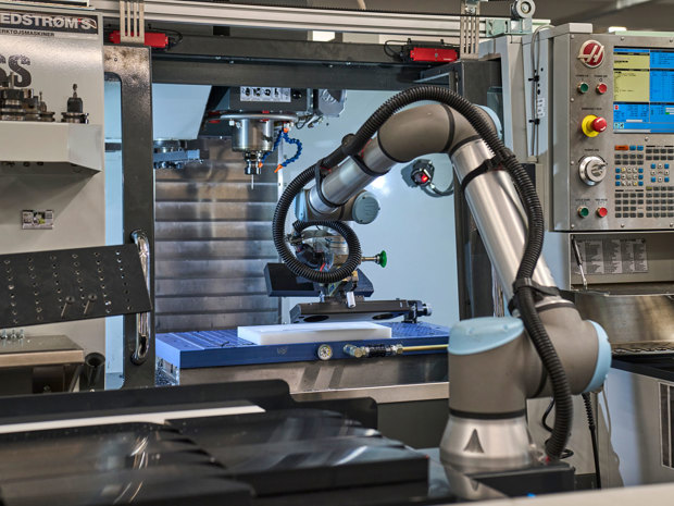 A robot with one arm turns a plastics part in a CNC milling machine.
