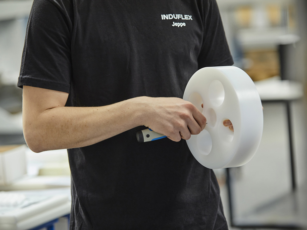 Drejet emne med fire huller i hvid POM afgrates manuelt af Induflex' industritekniker