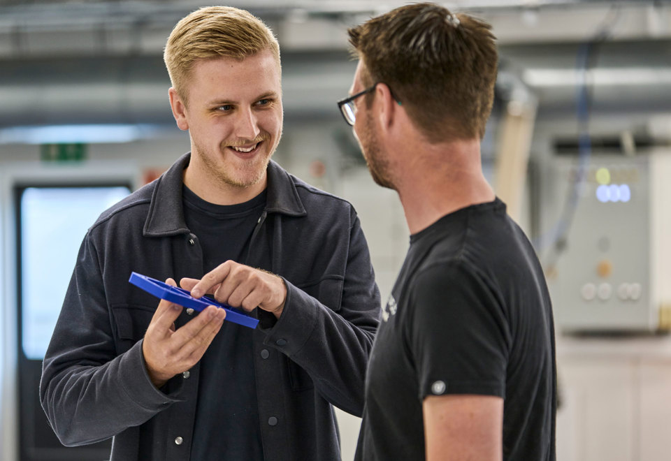 En sælger peger på et blå plastemne foran en industritekniker. 