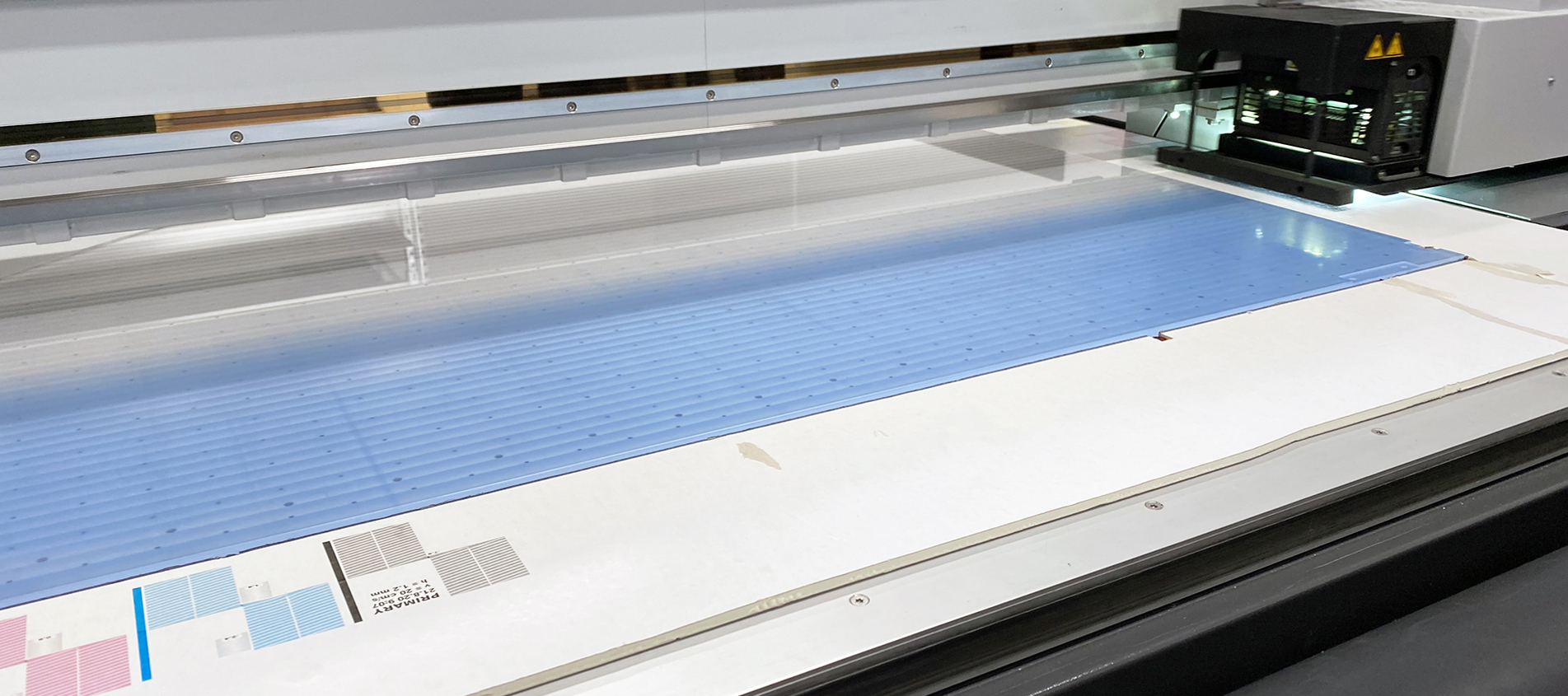 Digital printer printing a light blue print on a clear sheet of acrylic