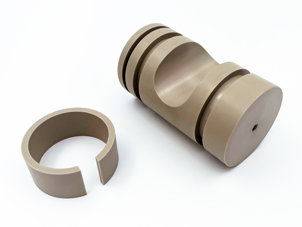 To CNC-drejede emner i PEEK på en hvid baggrund.