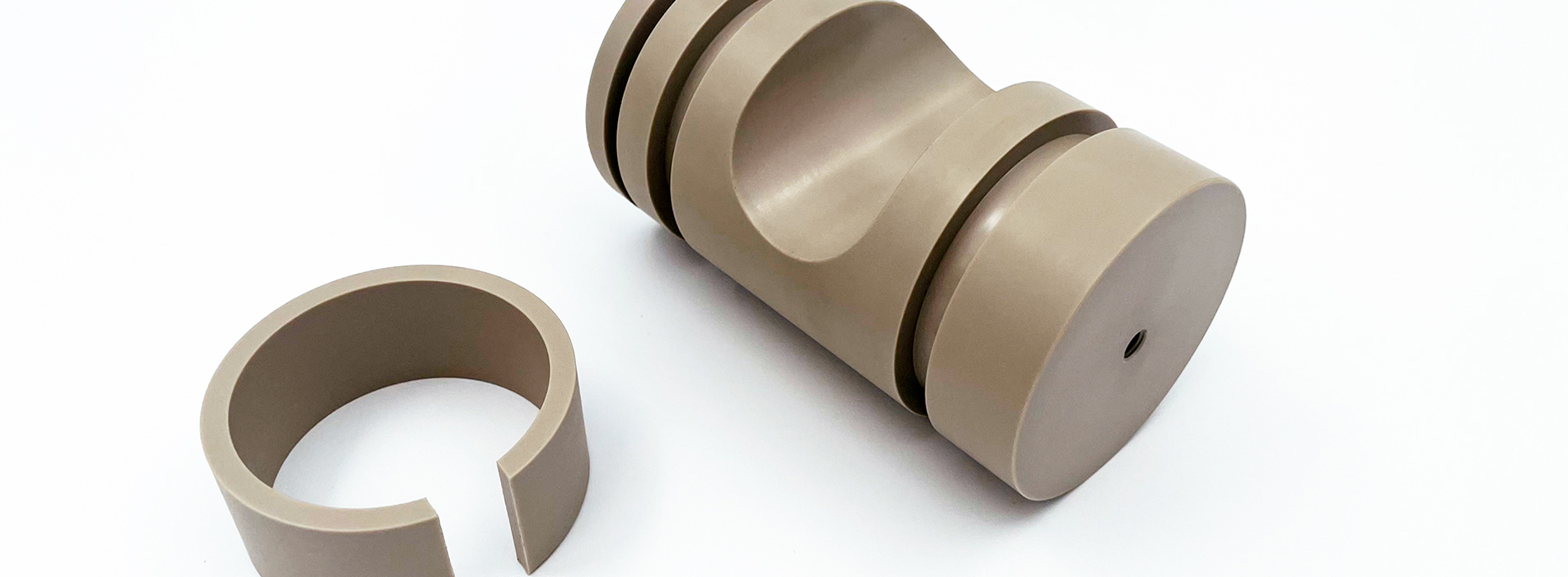 To CNC-drejede emner i PEEK på en hvid baggrund.