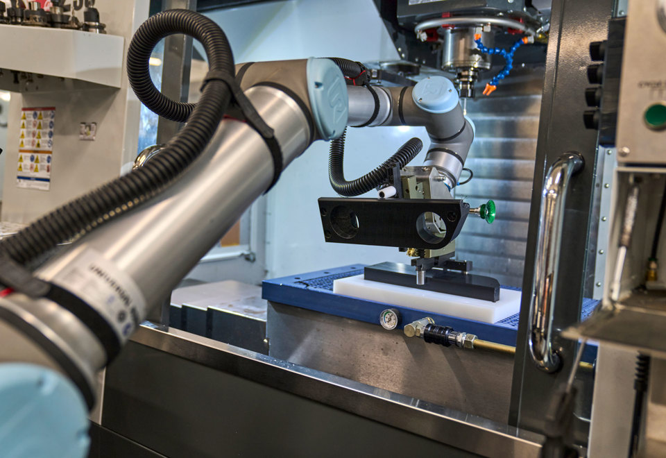 En robot med en arm indsætter et sort plastemne i en CNC-drejebænk. 