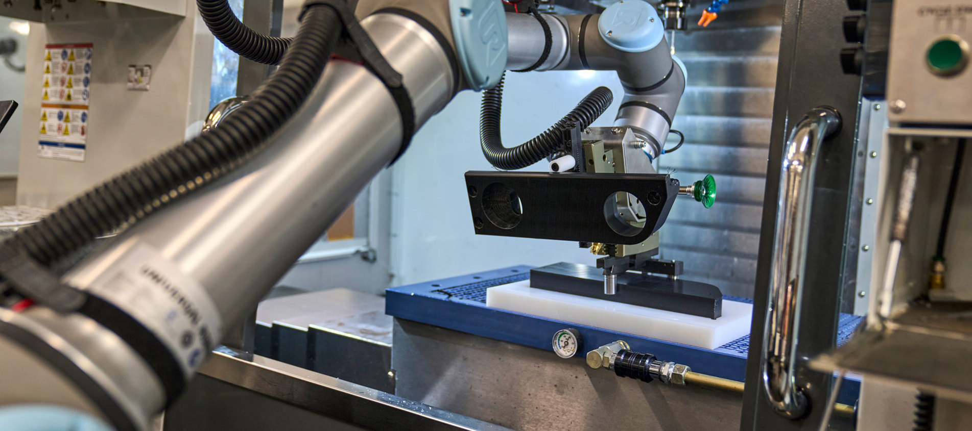 A robot with one arm inserts a black plastic part in a CNC turning machine.