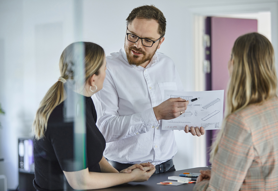 Tre sælgere hos Induflex diskuterer detaljer på en teknisk tegning af et plastemne til en kunde