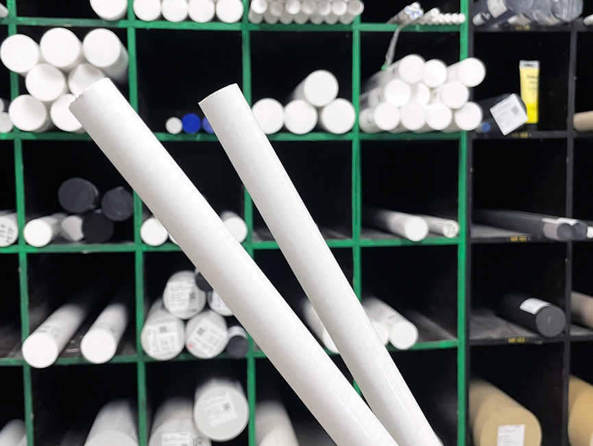 Two white rods of PET-P in stock with several rods on shelves behind them