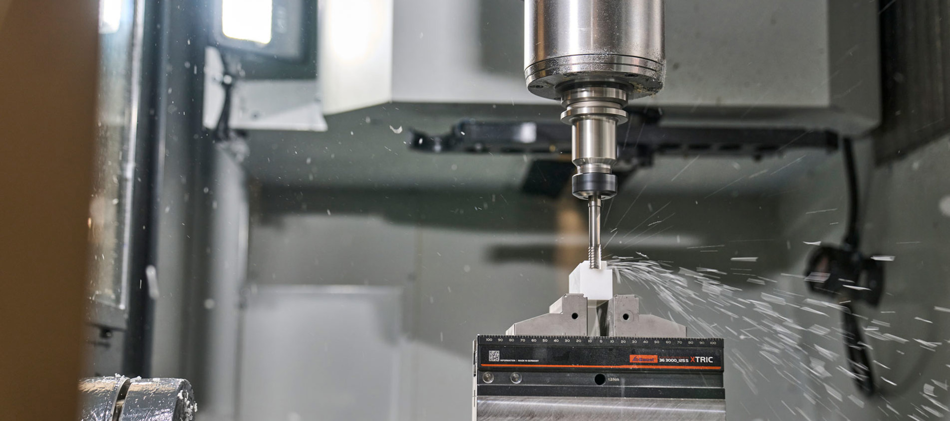 A white machine part in plastics is being milled in a five-axis milling cutter.