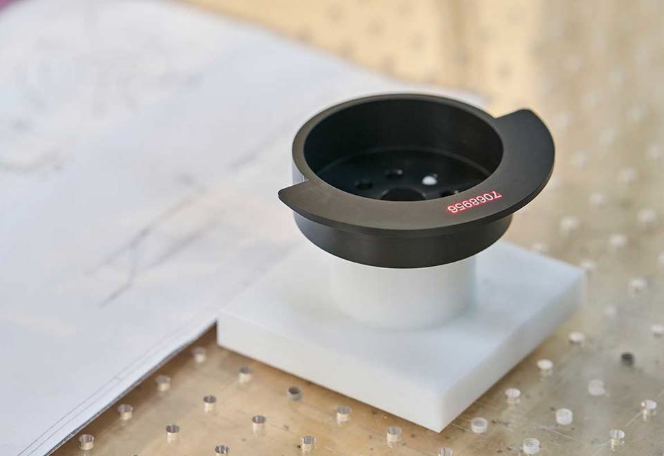 A black turned machine part with laser engraved numbers.