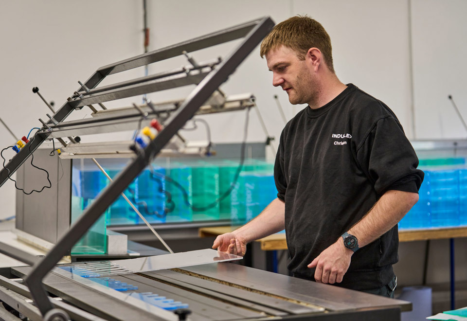 En medarbejder justerer et akrylstykke som ligger på et varmbukke-bord.