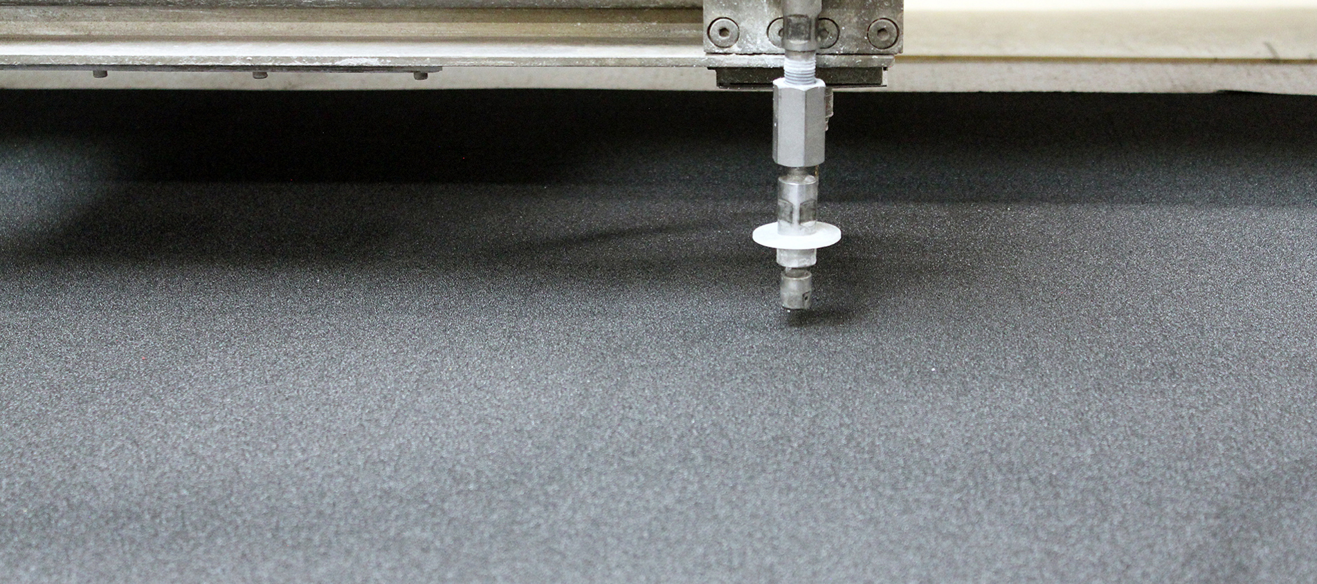 Water-jet on a water-jet cutter cutting through a sheet of black rubber