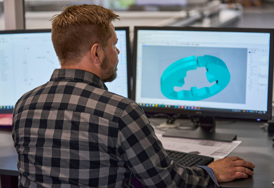 En teknisk designer finjusterer et design af en maskindel i plast på sin computerskærm.