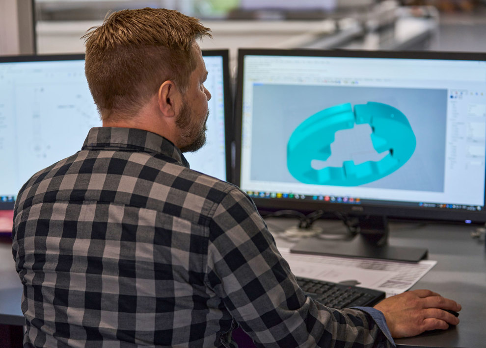 A technical designer adjusts a design of a machine part og plastics on his computer screen.