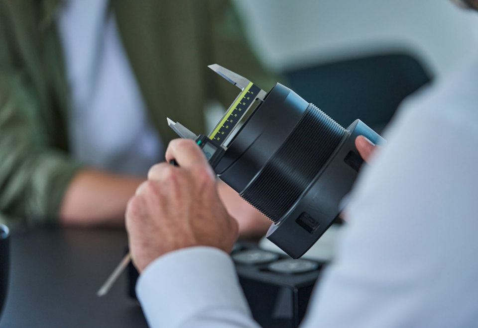 En sort drejet maskindel i plast måles med en skydelære. 