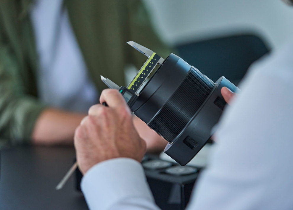 En sort drejet maskindel i plast måles med en skydelære. 