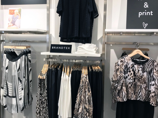 Logoskilt i sort akryl står på reol i tøjbutik