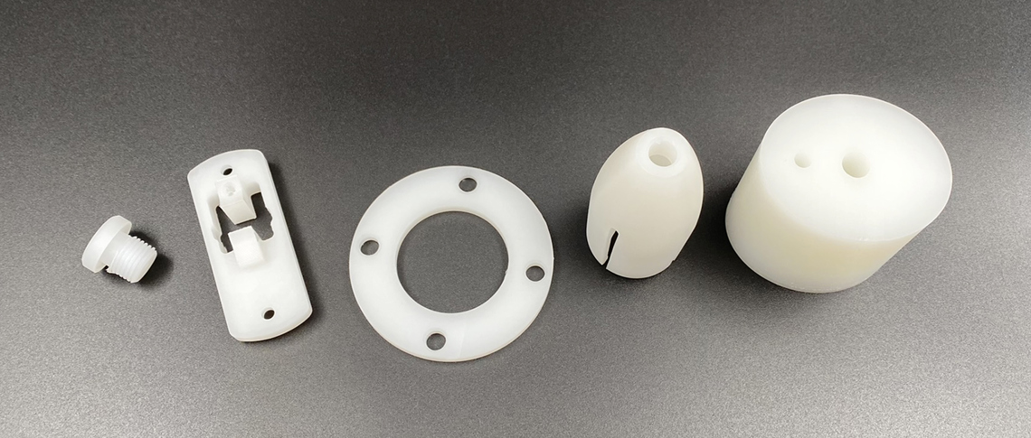 Hvide maskindele af PVDF ligger på en række på en sort baggrund.