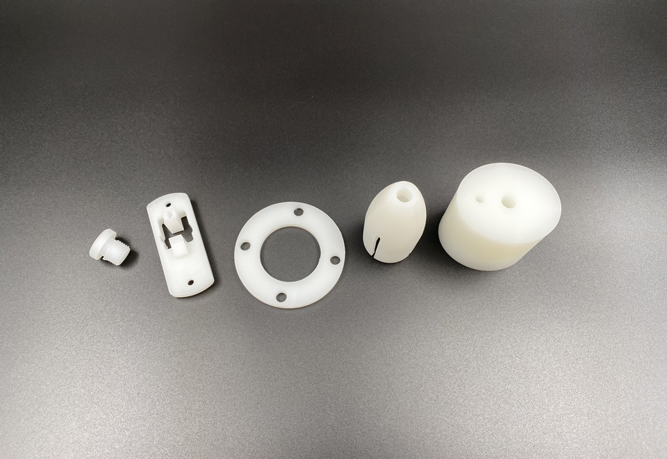 Hvide maskindele af PVDF ligger på en række på en sort baggrund.