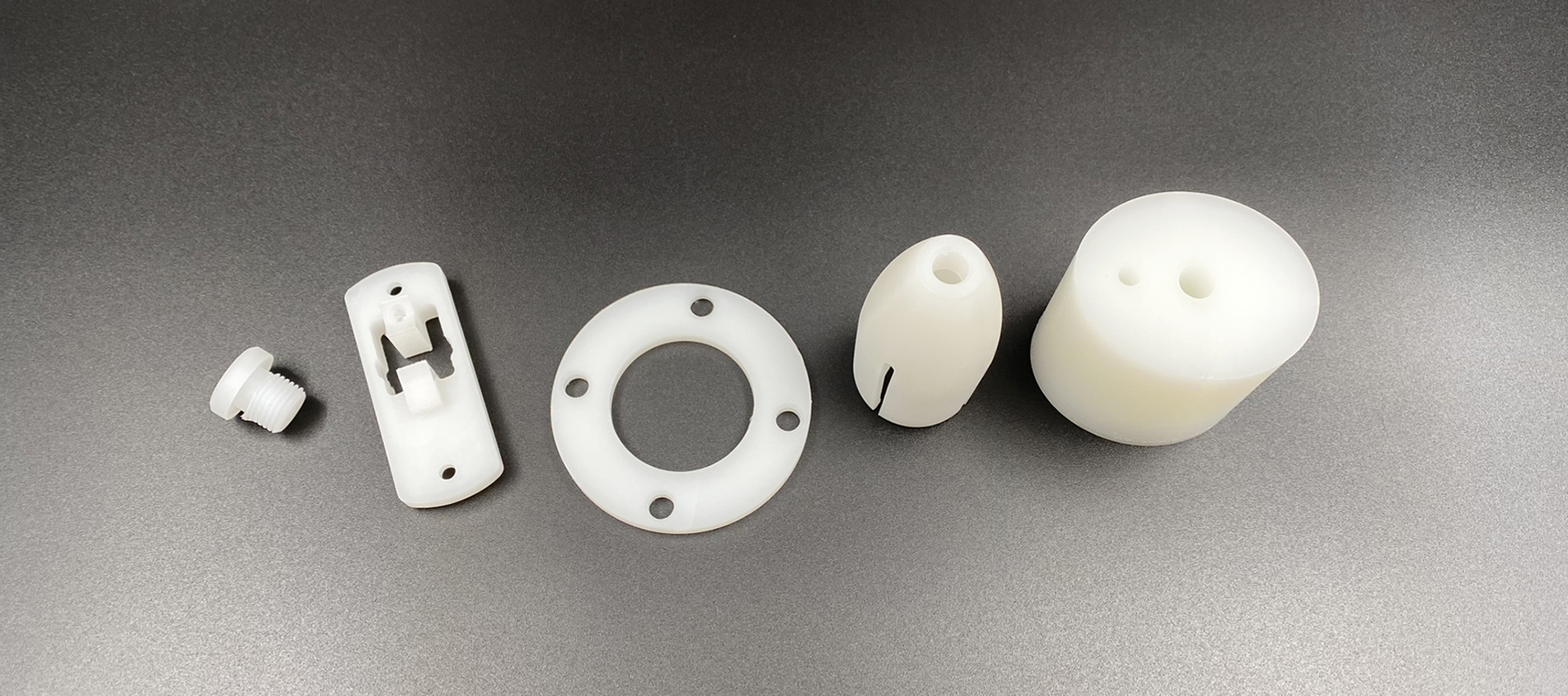 Hvide maskindele af PVDF ligger på en række på en sort baggrund.