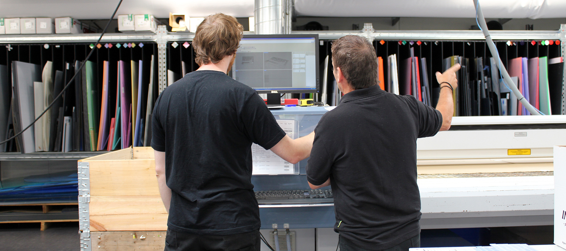 Two industry technician looking at the screen by a laser cutter, they are in the middle of preparing