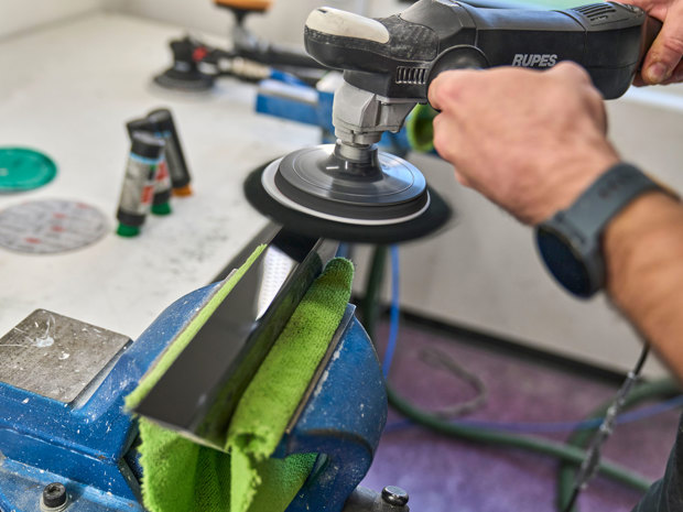A piece of black acrylic is being polished manually using a polishing machine.