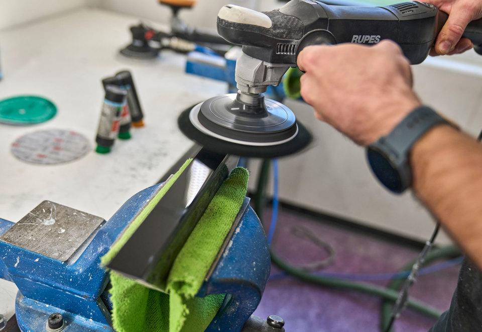 A piece of black acrylic is being polished manually using a polishing machine.